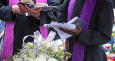 Image showing a Christian funeral service in a church, with mourners gathered around a casket adorned with flowers. The minister leads the service, offering prayers and comforting words to the grieving family and friends. The atmosphere is solemn and reflective, conveying a sense of faith, hope, and the journey towards eternal peace